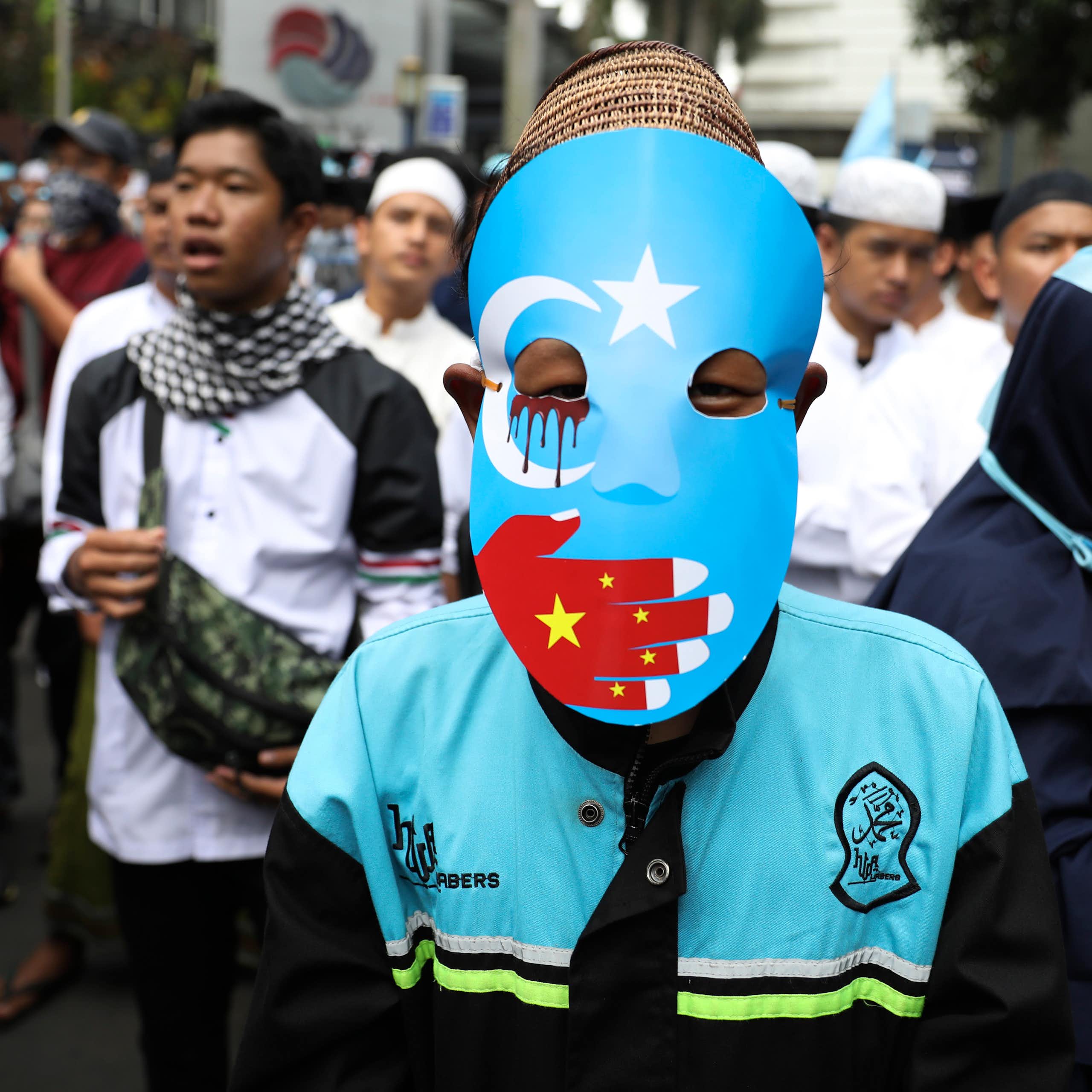 A protestor in a blue mask with a red hand over the mouth.