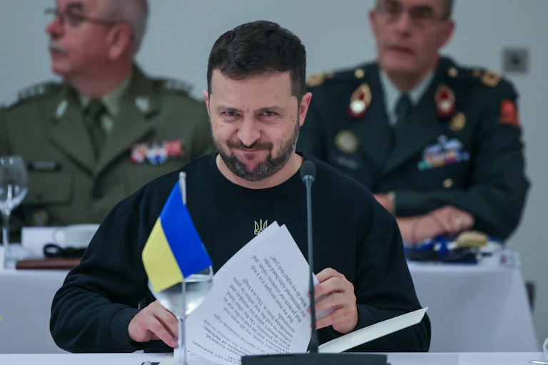 Ukrainian president, Volodymyr Zelensky looks through papers while sitting behind a Ukrainianflag..