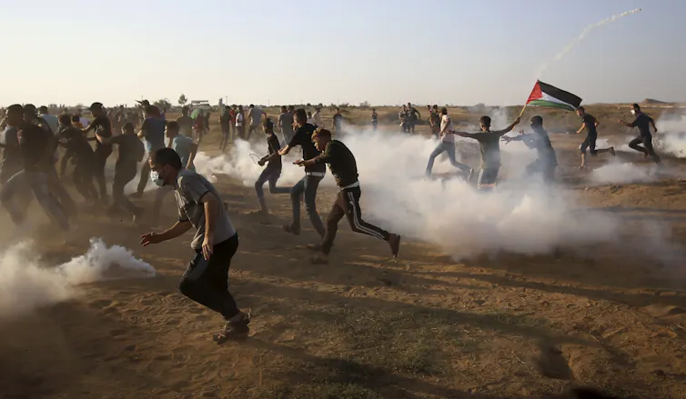 Protesters flee in a dusty open field while being sprayed with teargas.