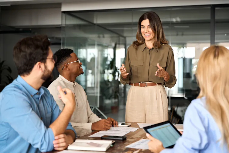 A young woman standing and speaking to a group of people seated at a conference table
