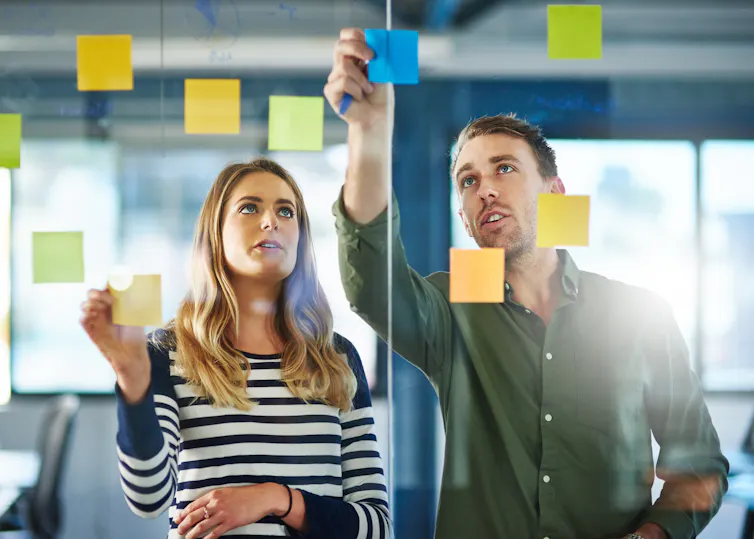 A man and a woman look at sticky notes posted on a glass wall