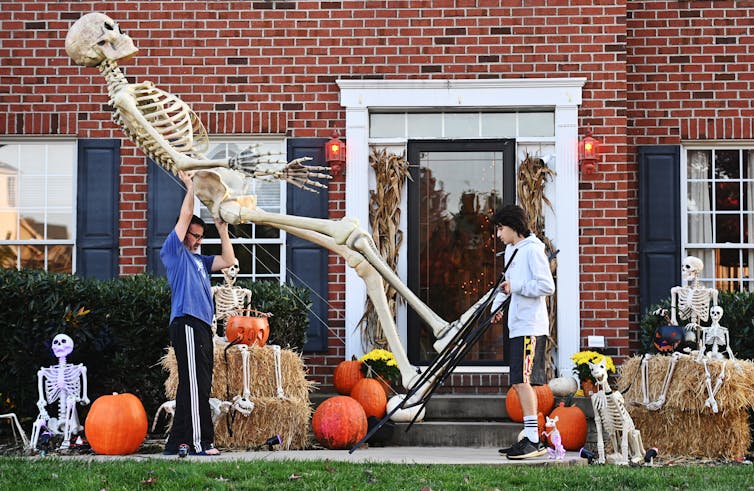 A father and son are photographed outside their home, carrying a 12-foot decorative skeleton from Home Depot.