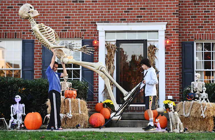 A father and son are photographed outside their home, carrying a 12-foot decorative skeleton from Home Depot.
