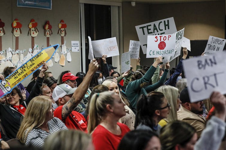 Audience members hold up signs for and against critical race theory