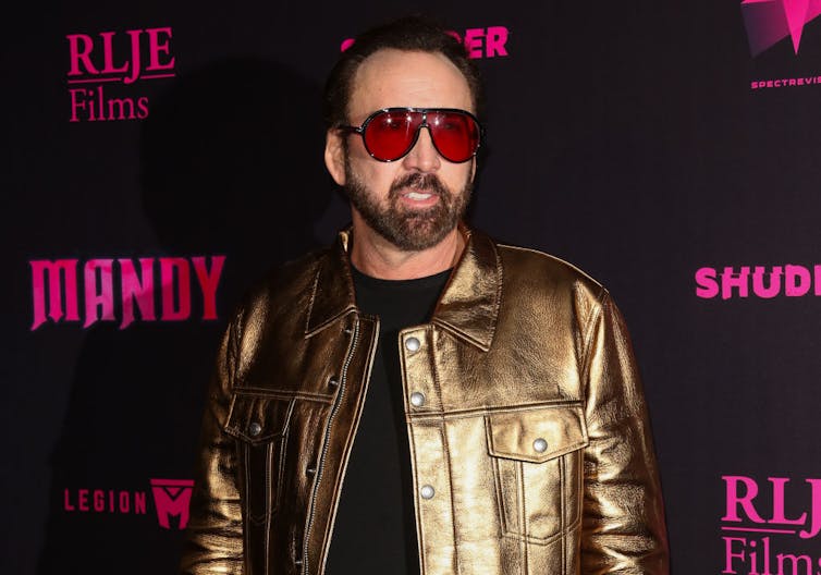 Man with beard poses while wearing a gold jacket and aviator sunglasses.