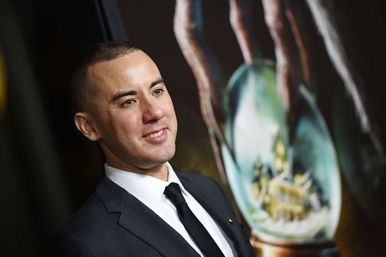 Young man with closely cropped hair wears black suit and black tie.