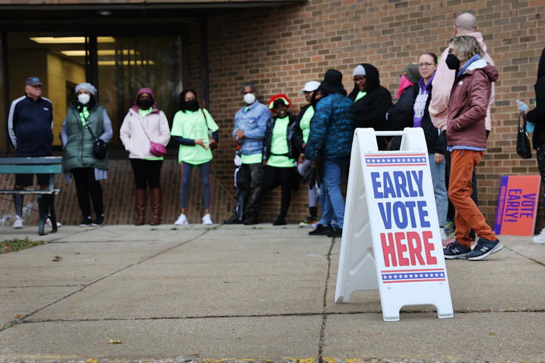 People stand outside a brick building near a sign reaading 'early vote here'