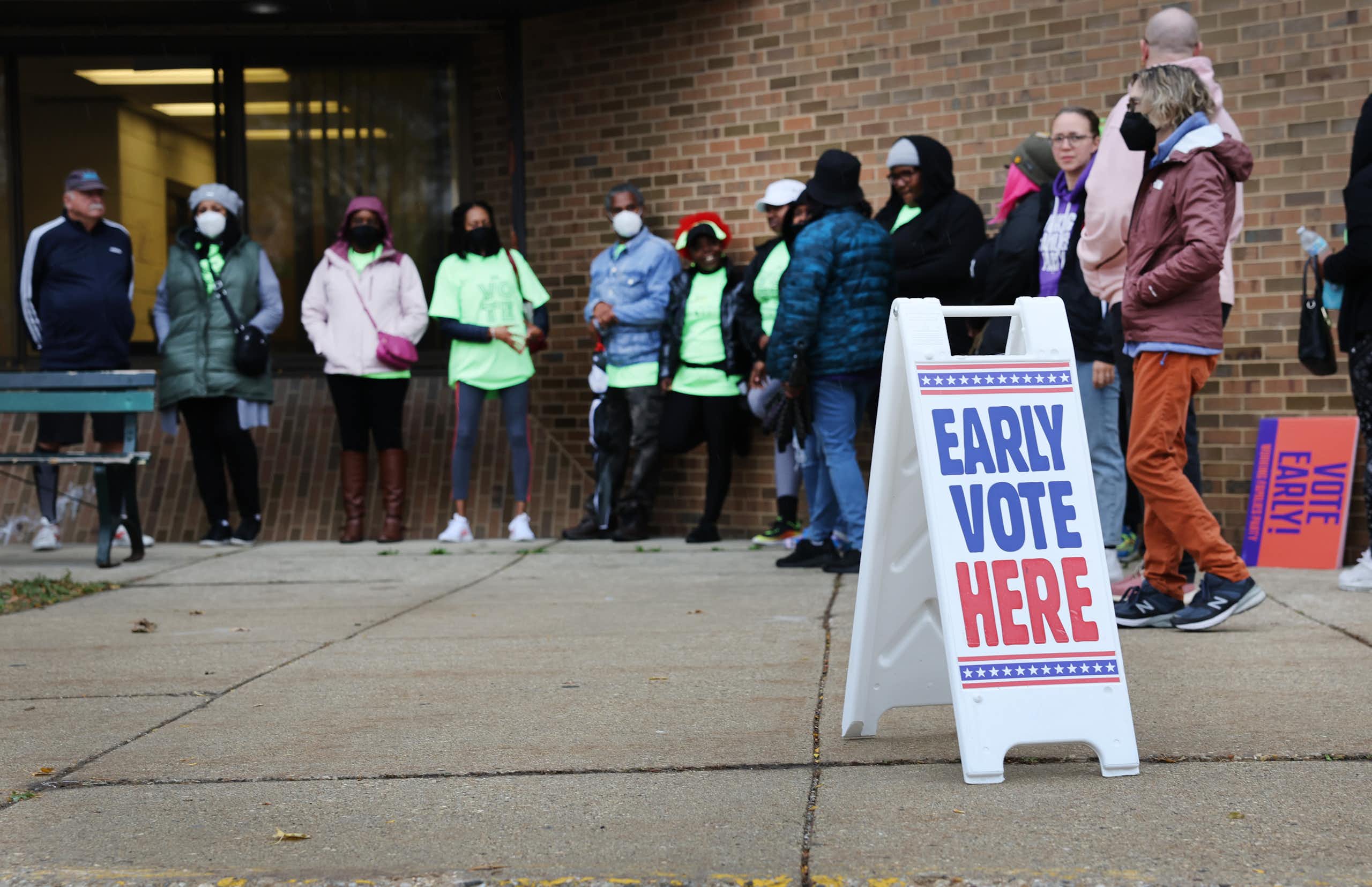 People stand outside a brick building near a sign reaading 'early vote here'