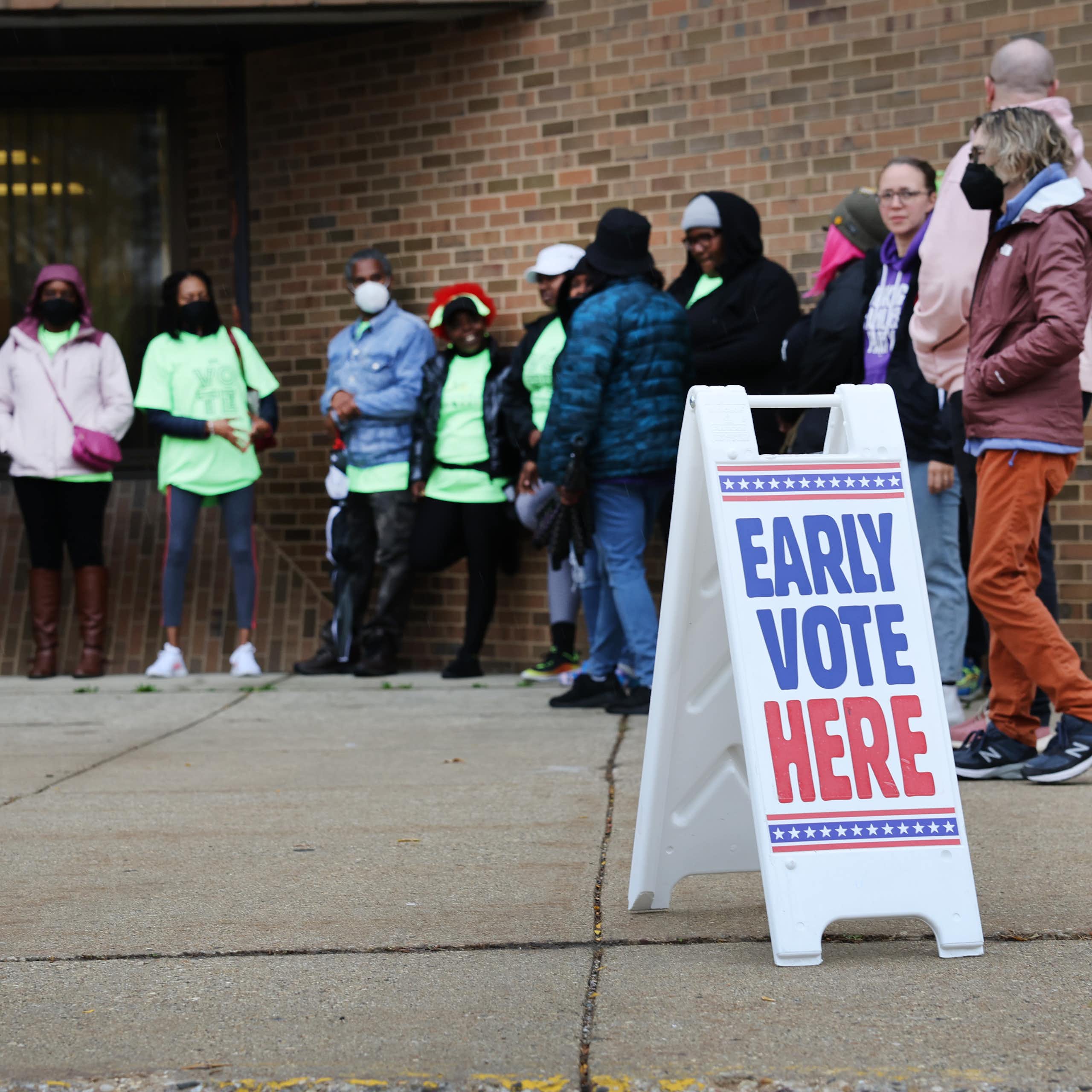 People stand outside a brick building near a sign reaading 'early vote here'