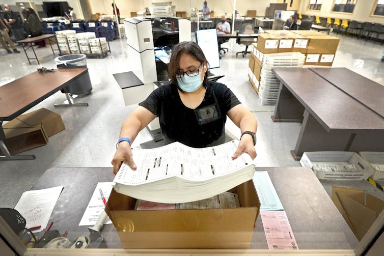 a woman holds a stack of large paper forms at a table in a large room