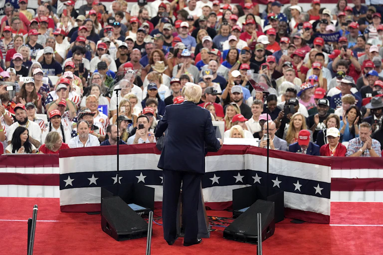 A man in a suit addresses a large crowd wearing red caps