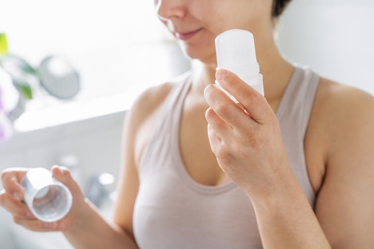 Woman with antiperspirant in one hand, reading the lid in the other