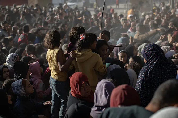 Three little girls stand up in a sea of people waiting for aid.