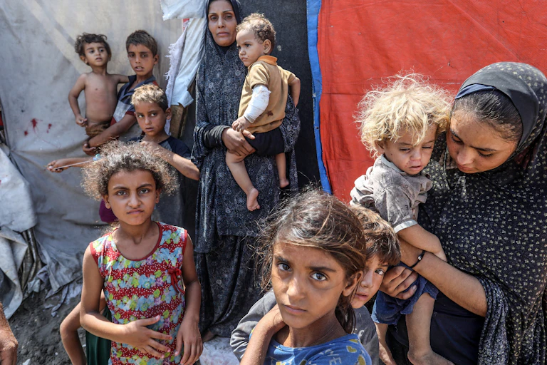 A group of thin children stand outside a tent in Gaza.