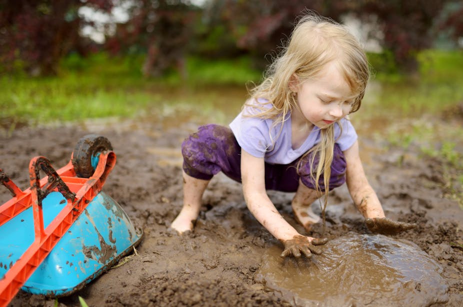A young child plays in the mud outside.