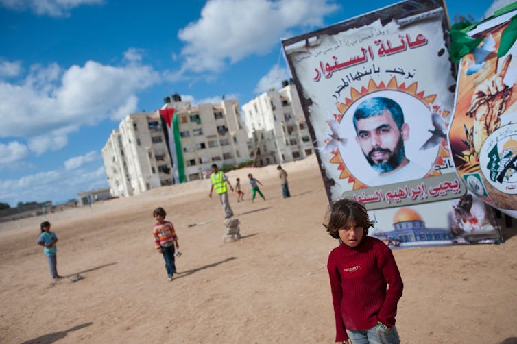 Children are seen playing on a dirt field in front of a banner showing a man's face.
