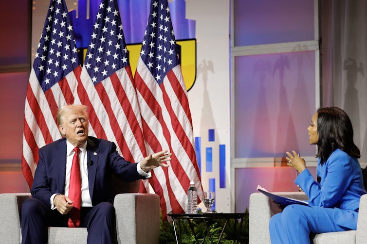 Donald Trump sits next to a journalist on stage.