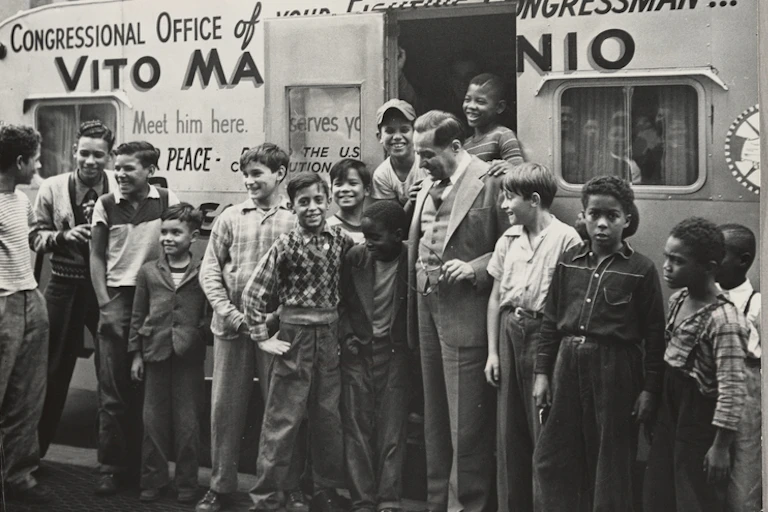 Marcantonio is surrounded by young men in front of his office.