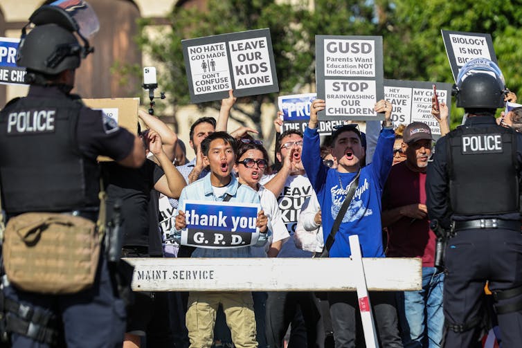 People shout and hold signs aloft indicating their disapproval of trans rights in schools.