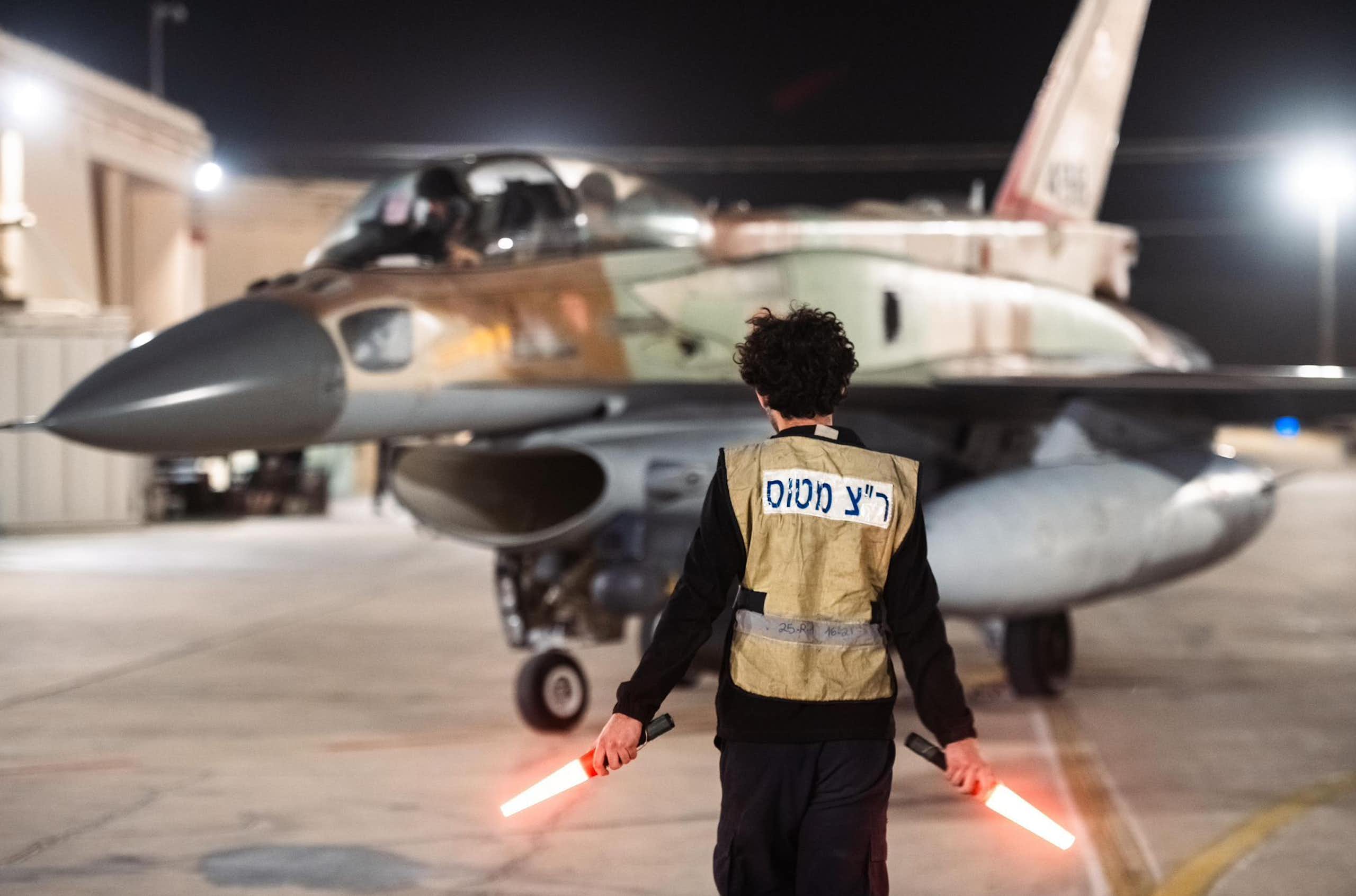 A man with hand-held lights stands in front of a military jet.