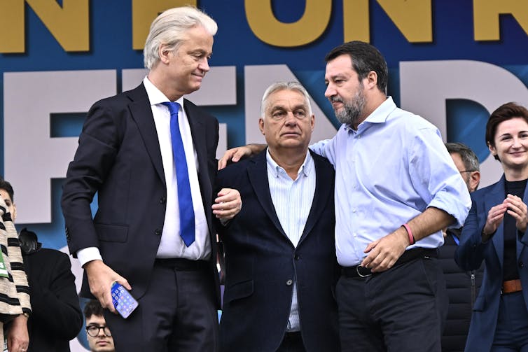 Geert Wilders, Viktor Orban and Matteo Salvini standing arm-in-arm on stage.
