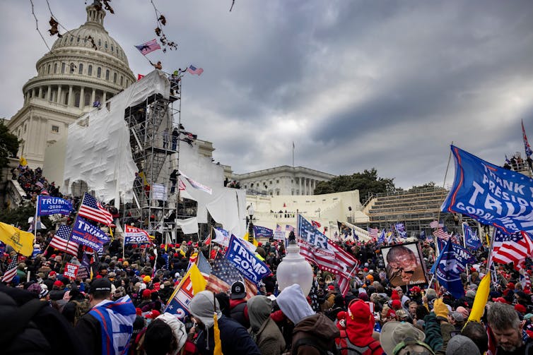 A mob of people storming up to a large white building, holding flags and signs.
