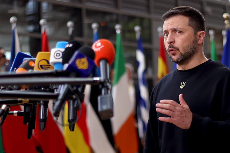 Volodymyr Zelensky talking into a bank of microphones.