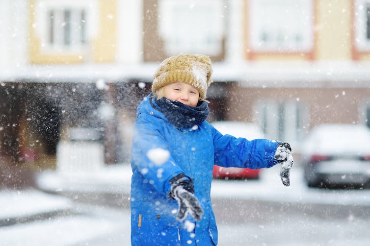 A young child throws a snowball in a carpark.
