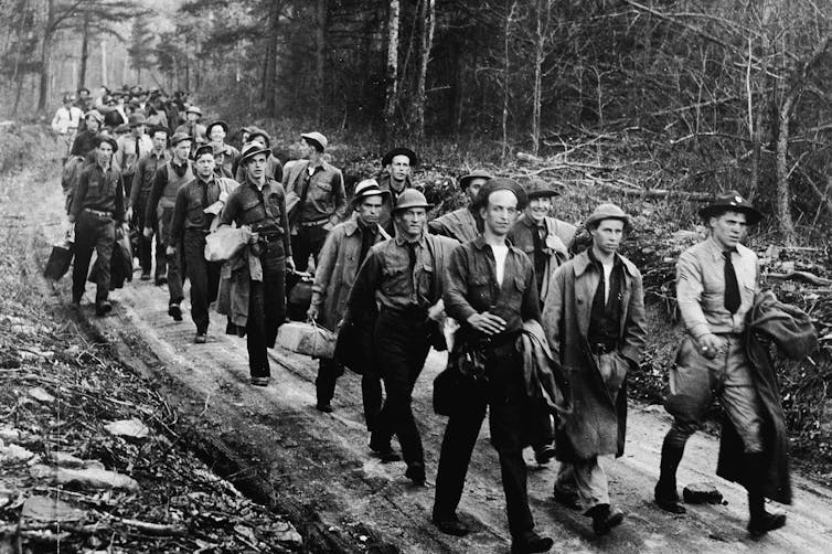 Dozens of men walk along trail in a forest.