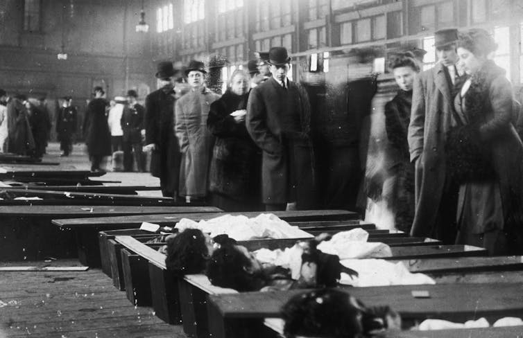 People walk by open coffins on a factory floor.