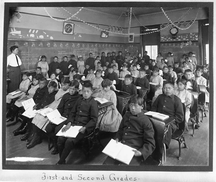 A black and white photo shows students seated in rows in a classroom, while the instructor is standing in front.