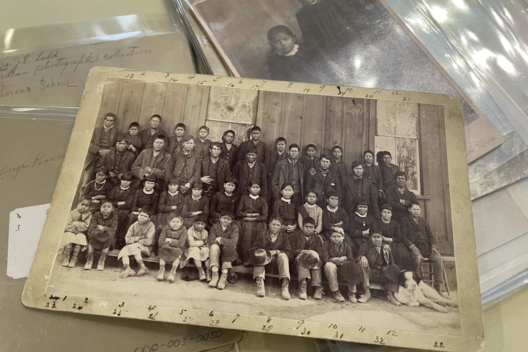 Yellowed class photographs of Indigenous students placed on top of others, one of which shows two young girls.