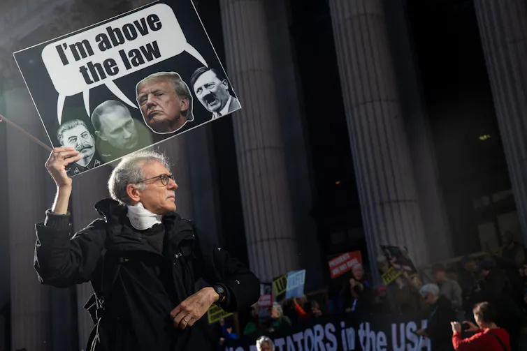 A protester holding a sign featuring Donald Trump and Adolf Hitler and a caption, reading 'I'm above the law'.