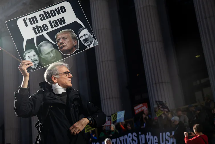 A protester holding a sign featuring Donald Trump and Adolf Hitler and a caption, reading 'I'm above the law'.