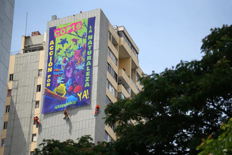 Activists in orange jumpsuits abseil down a building to unfurl a colourful banner