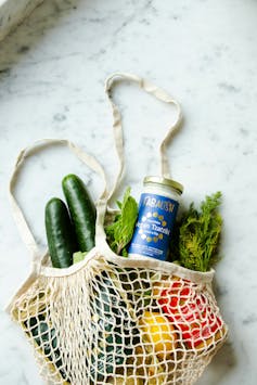 A bag full of groceries including lemons, cucumber and herbs