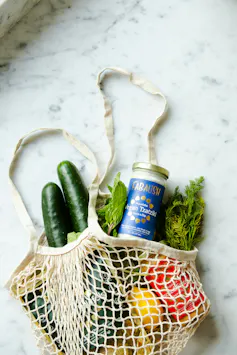 A bag full of groceries including lemons, cucumber and herbs