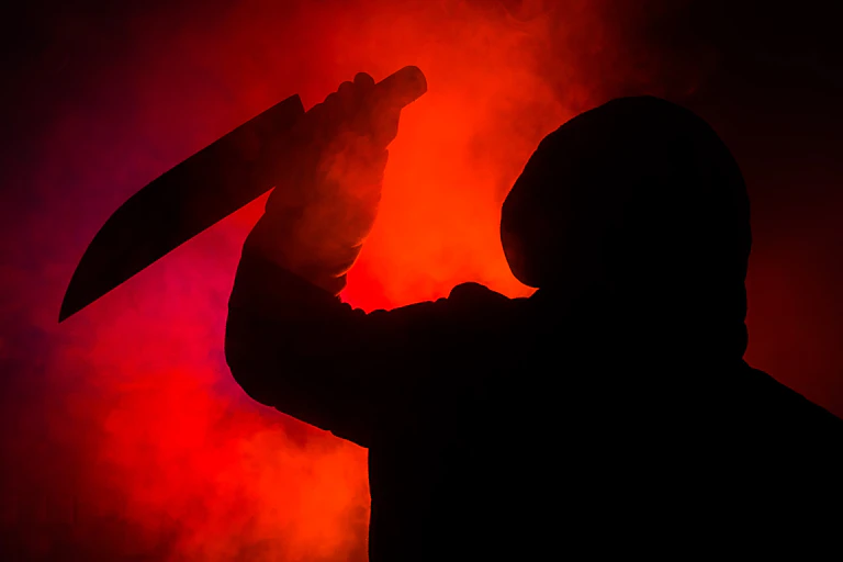 A shadowy figure in a hood and holding a knife stands against a red and black background.