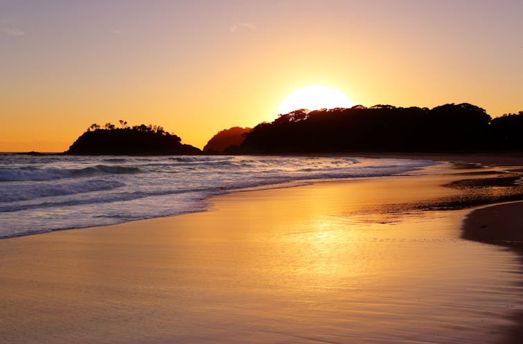 The golden sun rises behind the headland and detached island at Number One Beach, Seal Rocks NSW.