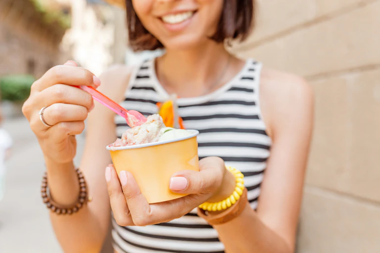 Young woman dipping spatula into tub of ice cream or gelato