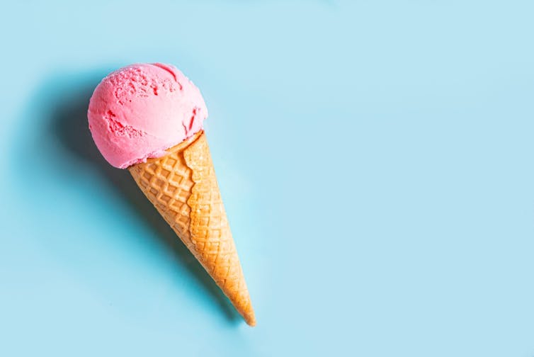 Pink ice cream in cone against blue background