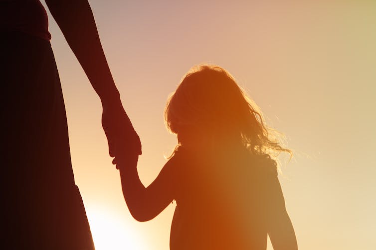 The silhouette of a young girl holding onto a hand