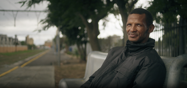 A man sits on a bench at a railroad.