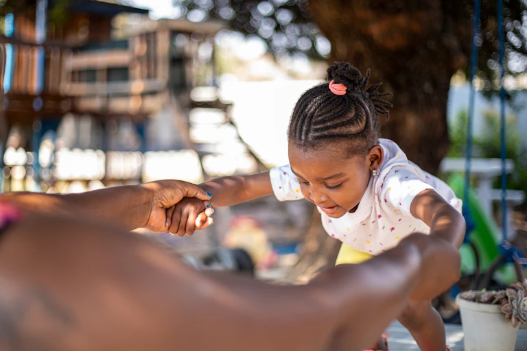 A little girl looking down as she prepares to jump with her mother's help.