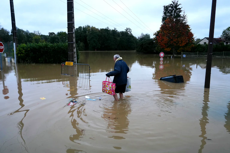 vieille dame qui porte ses courses les pieds dans l'eau des inondations