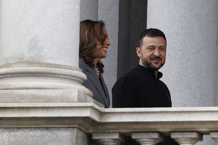 A man and a woman walk along a balcony.