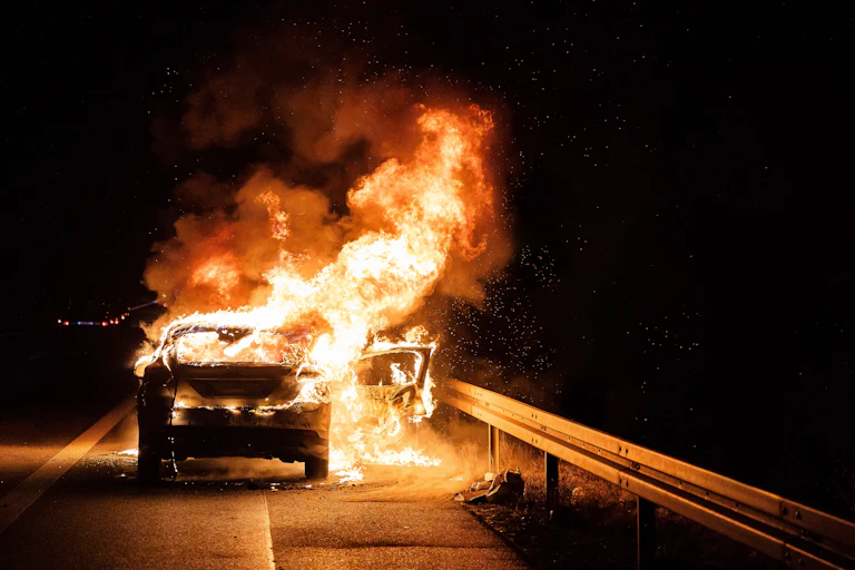 Une voiture en flammes au bord de la route.