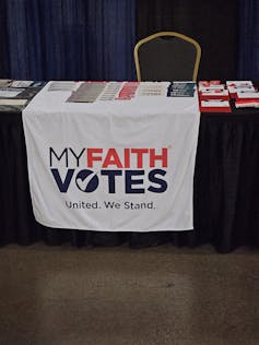 A white poster hanging on the side of the table says 'My faith votes.'