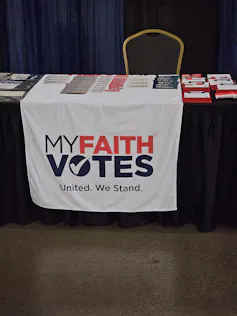 A white poster hanging on the side of the table says 'My faith votes.'
