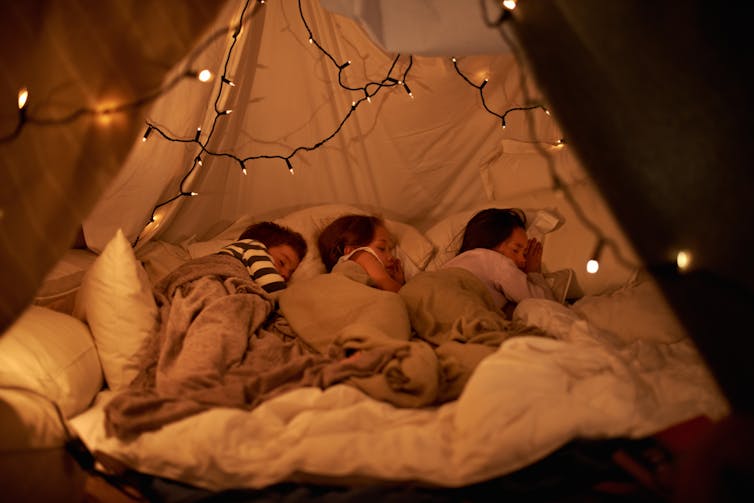 Three young children asleep in a tent fort